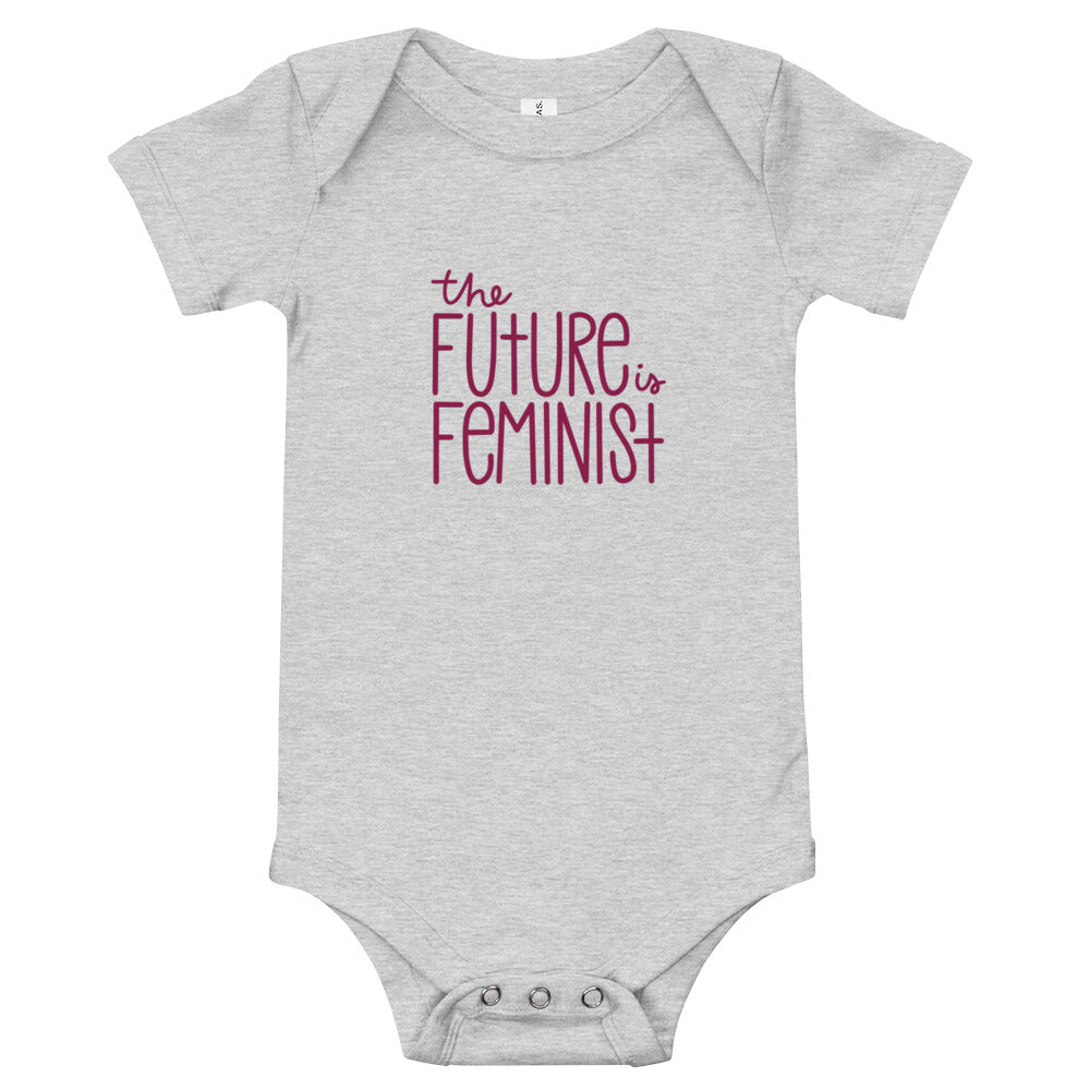 Grey infant onesie with the text "The future is feminist" printed on the center of the chest in ruby font. On the back, in the center just below the neckline is a black The SHE Mark logo with the words "The SHE Mark" printed below it in black.