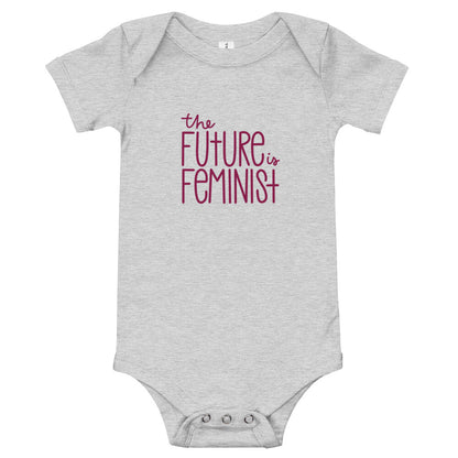 Grey infant onesie with the text "The future is feminist" printed on the center of the chest in ruby font. On the back, in the center just below the neckline is a black The SHE Mark logo with the words "The SHE Mark" printed below it in black.
