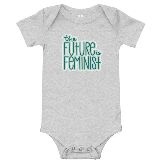 Grey infant onesie with the text "The future is feminist" printed on the center of the chest in teal font with a white outline. On the back in the center just below the neckline is a small The SHE Mark logo in white with the words "The SHE Mark" below it in white.