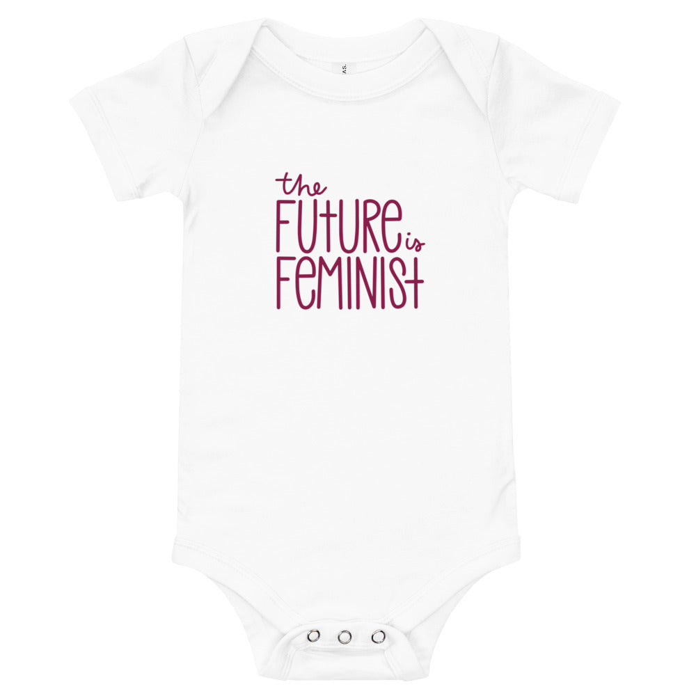 White infant onesie with the text "The future is feminist" printed on the center of the chest in ruby font. On the back, in the center just below the neckline is a black The SHE Mark logo with the words "The SHE Mark" printed below it in black.