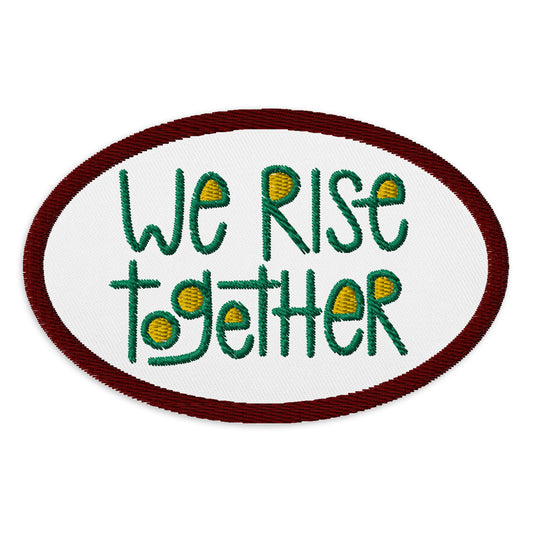 White patch with a ruby embroidered border. Centered on the patch reads "we rise together" in green embroidery with gold in the spaces of the letters.