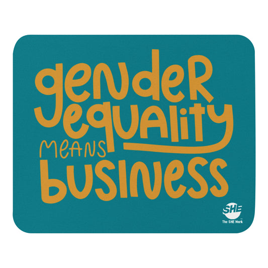 A teal mouse pad with "gender equality means business" in gold text. On the bottom right is a small, white The SHE Mark logo with "The SHE Mark" in white below it.