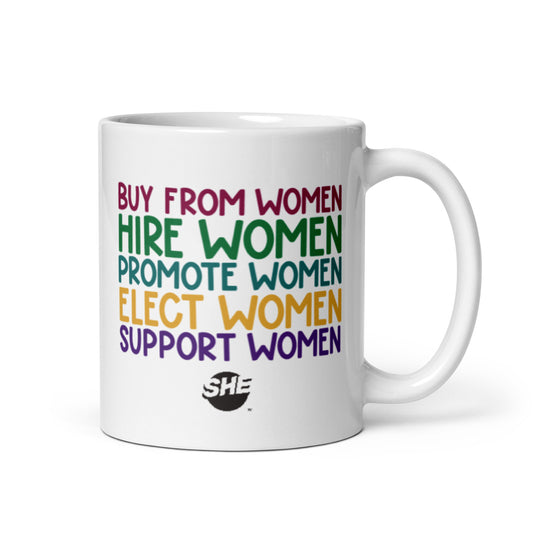 11oz white mug with "Buy from women" in ruby, followed by "Hire women" in green, "Promote women" in teal, "Elect women" in gold, and "Support women" in purple. The text is printed on the mug twice; once on each side so it's visible regardless of in which hand you hold the handle. Below the text is a black SHE Mark logo.